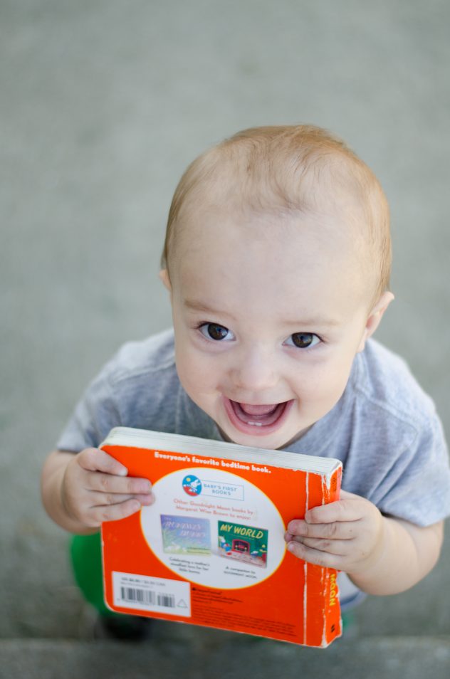 Finn smiling mischievously up at the camera as he holds his book up to his face like he's about to bite it.