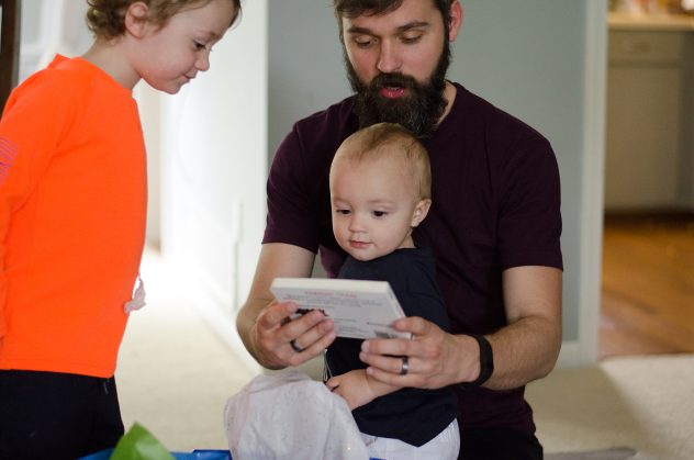 Finn, sitting in Daddy's lap as he helps him open presents and shows him the front of the train book he just opened