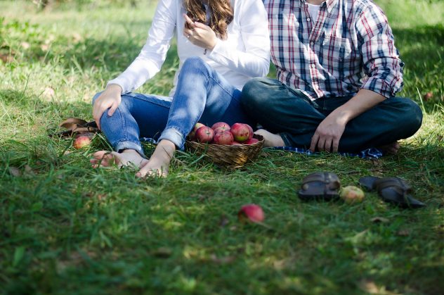 Photo of Sammy and Josiah sitting on the grass with their basket of apples and surrounded by apples. The photo shows just from the necks down.