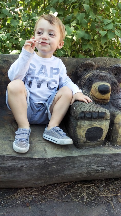 Miles sitting by the carved bear, eating his lollipop