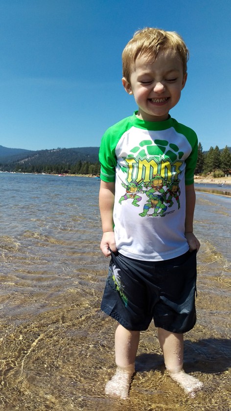 Miles squinting while he says cheese and stands in the shallow part of the lake by shore