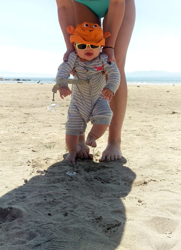 Finn looking at the camera while Brooke helps him feel the sandy beach under his toes