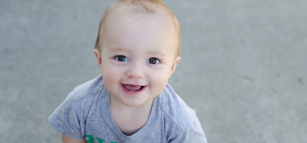 12 month photo of Finn toothy smile as he looks up at Mom with the camera