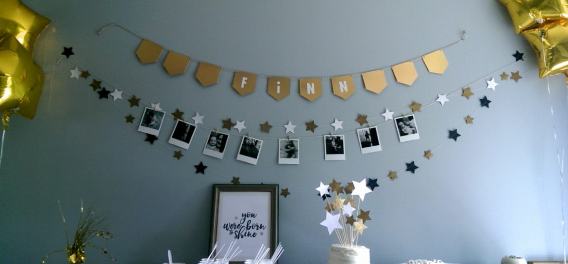 A wide shot of the cake table including the banners and garlands above and the gold star balloons on either end